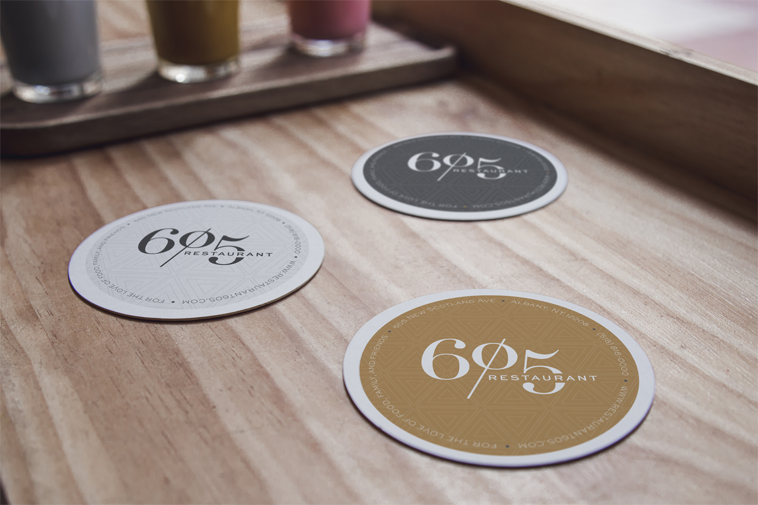 Three drink coasters featuring Restaurant 605 colors and logo on wooden table 